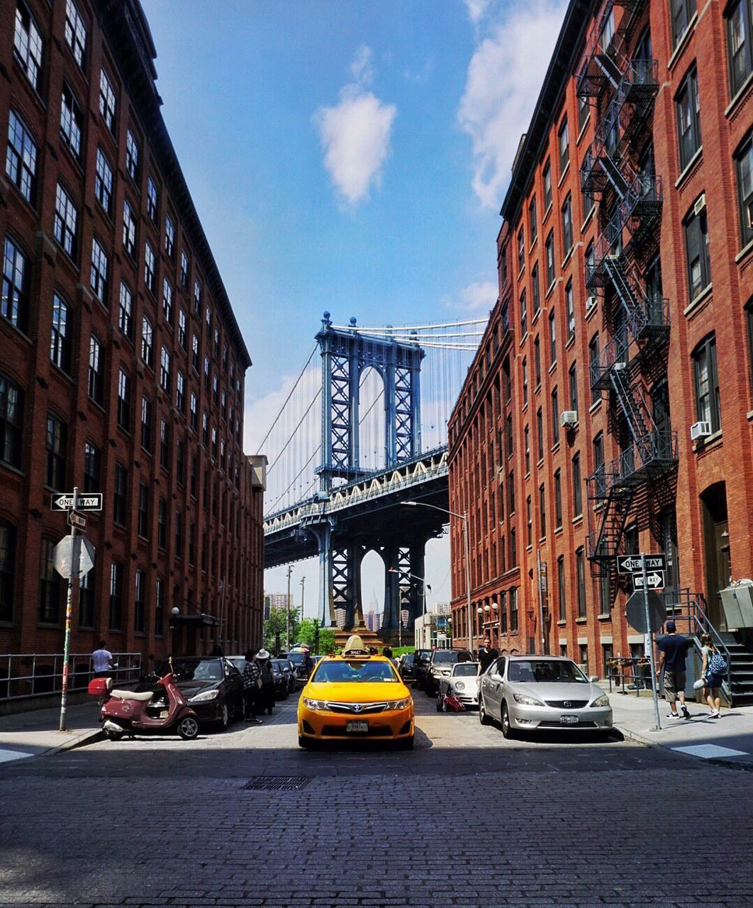 Cars on street amidst buildings against manhattan bridge in city