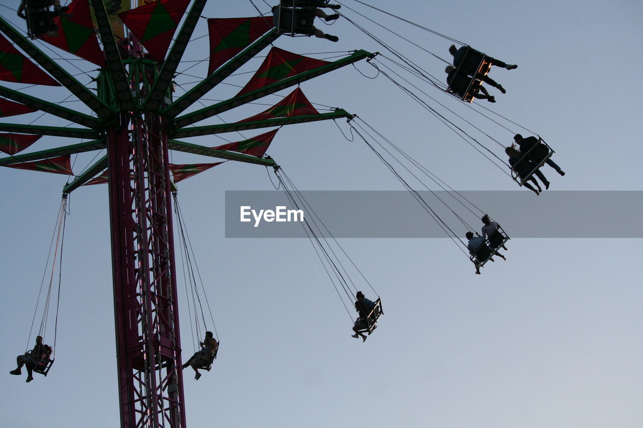 Low angle view of people on chain swing ride against clear sky