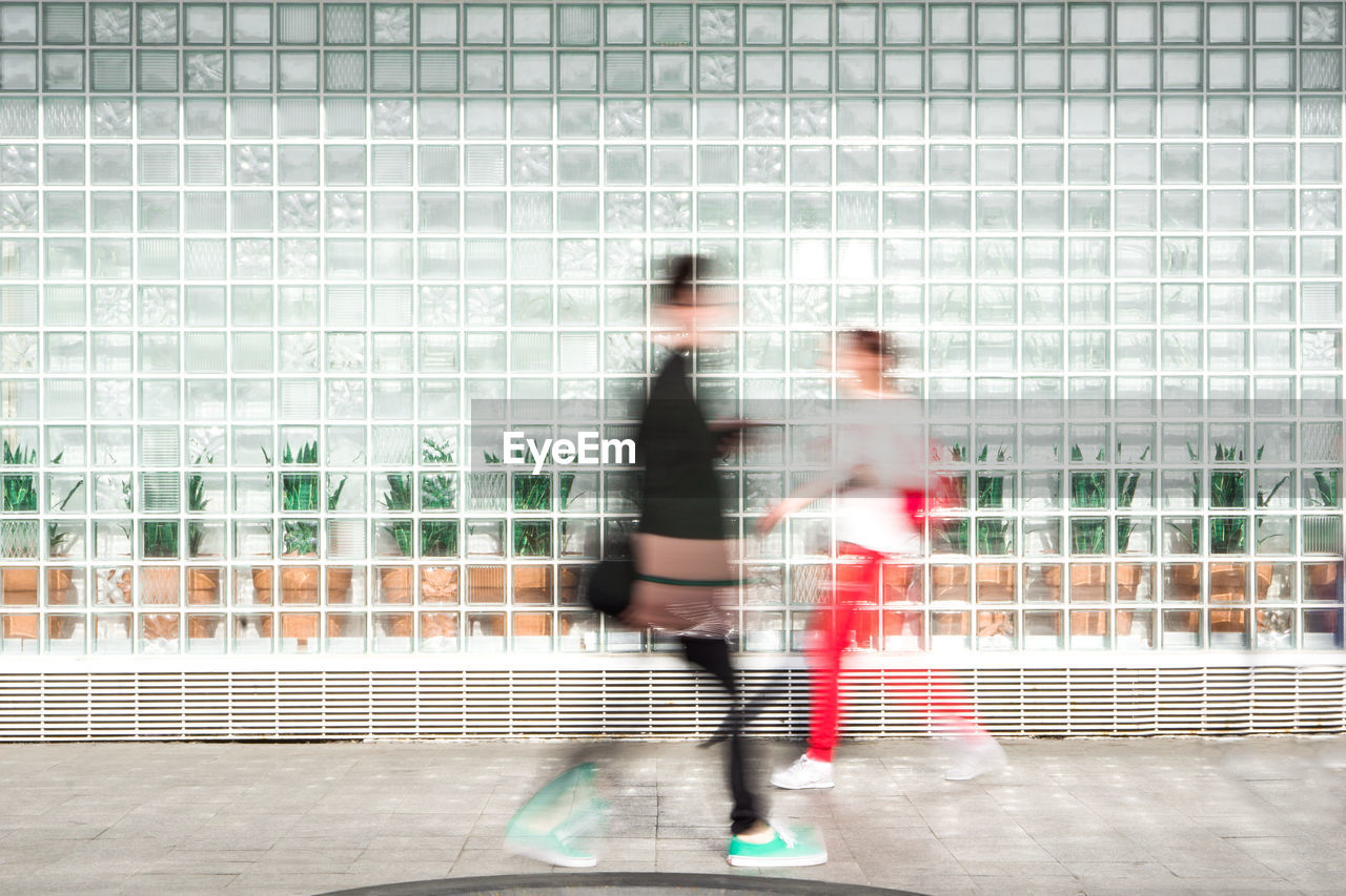 Blurred motion of man and woman walking against building