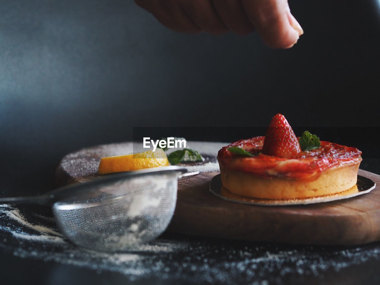 Cropped image of hand sprinkling sugar on strawberry tart