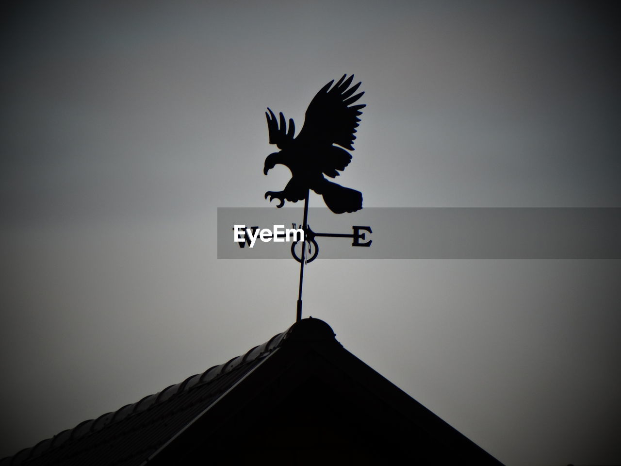 Low angle view of weather vane on roof against sky