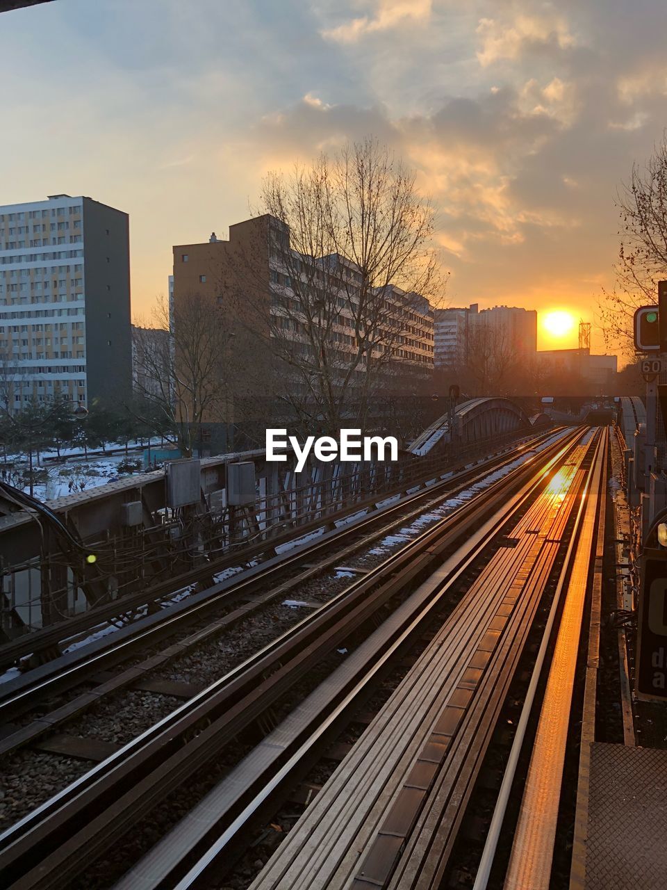 Railroad tracks by buildings in city during sunset