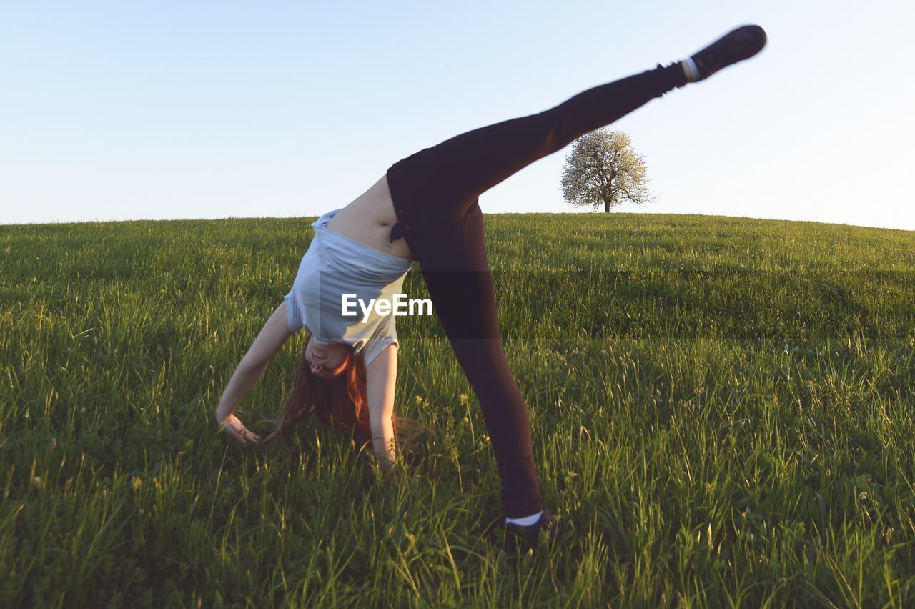 Full length of girl doing handstand on field against clear sky