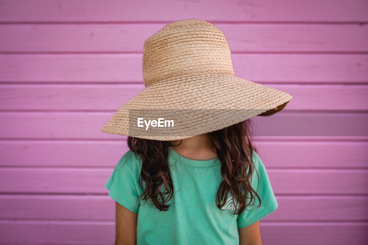 Portrait of little girl hiding her face under big straw hat