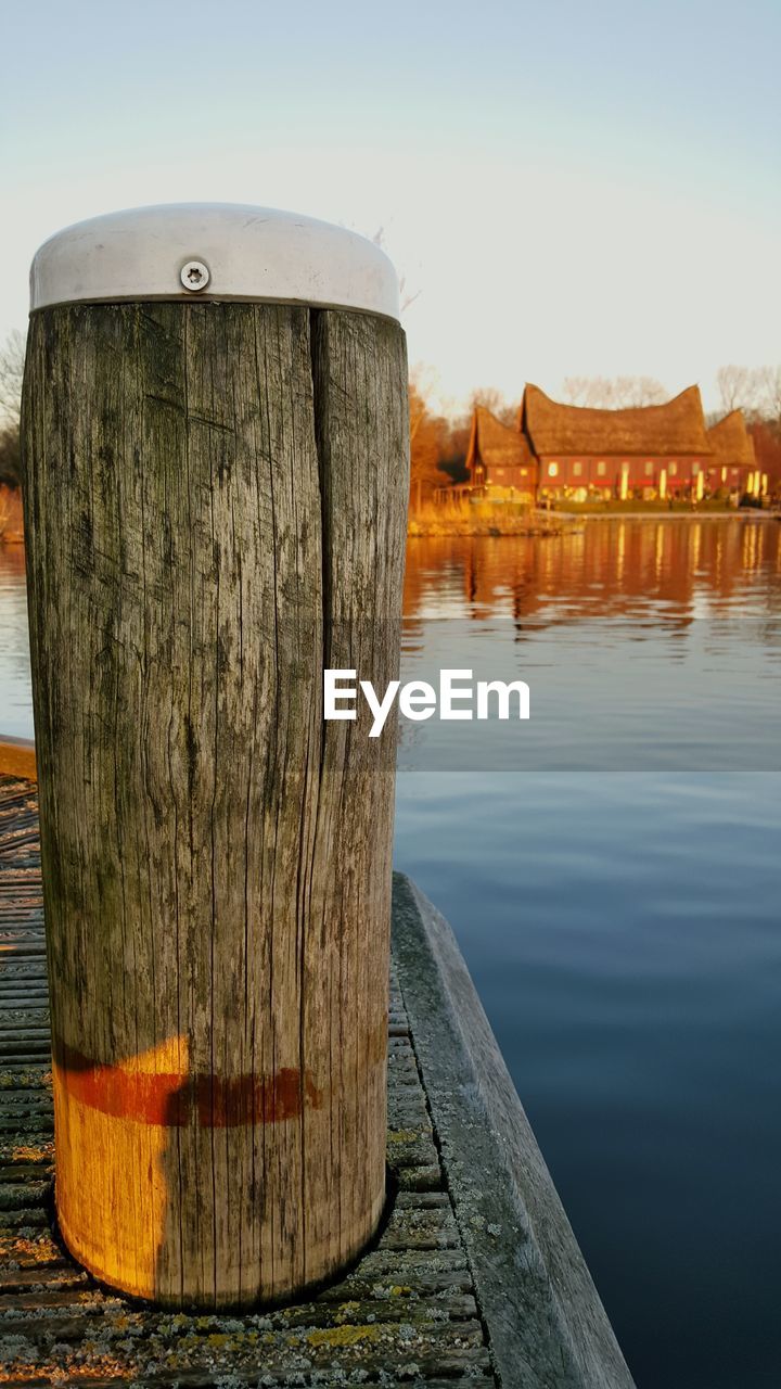 Wooden bollard on pier in lake against sky