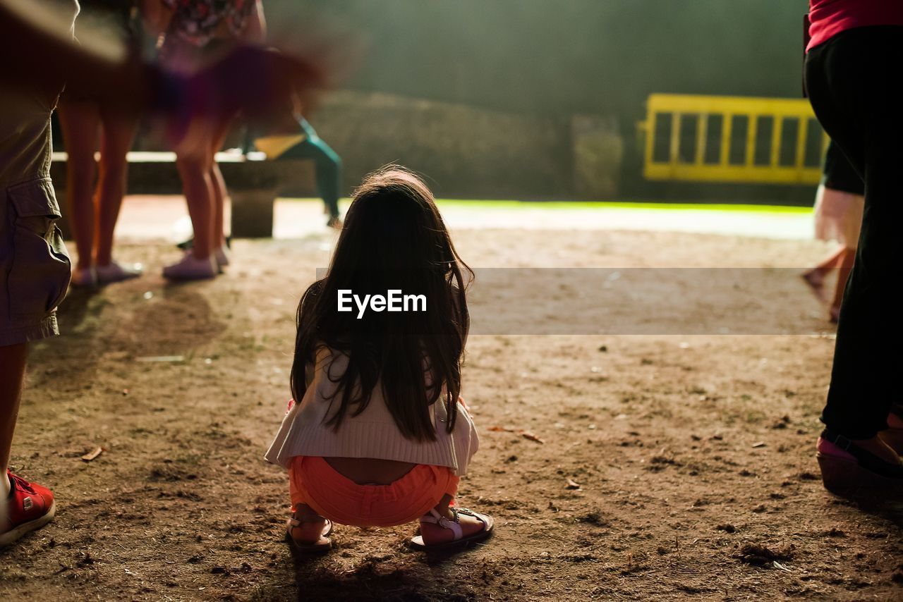 Rear view of girl crouching on field