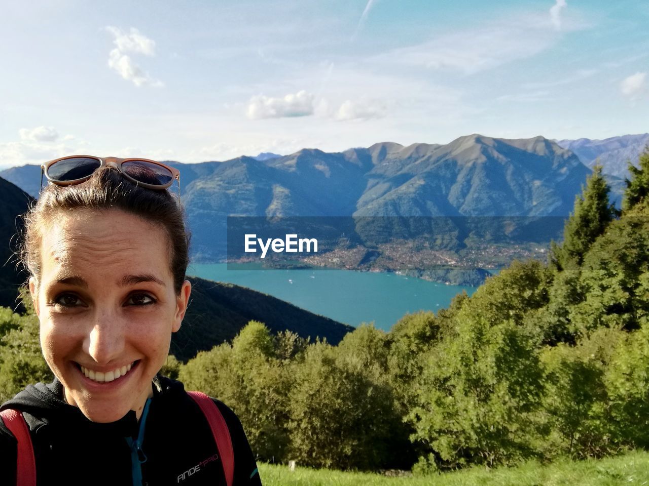 mountain, mountain range, looking at camera, real people, portrait, one person, leisure activity, sunglasses, day, nature, smiling, happiness, sky, outdoors, adventure, headshot, lifestyles, scenics, beauty in nature, young women, standing, young adult, tree, people