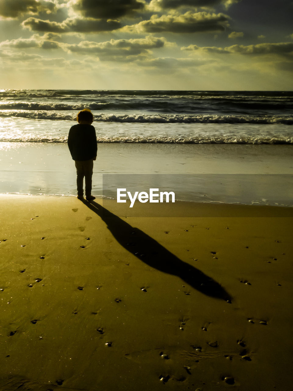 Boy standing at beach during sunset