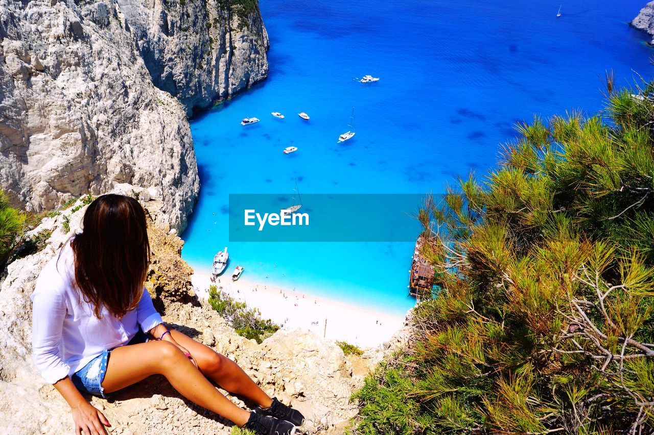 HIGH ANGLE VIEW OF WOMAN SITTING BY SEA