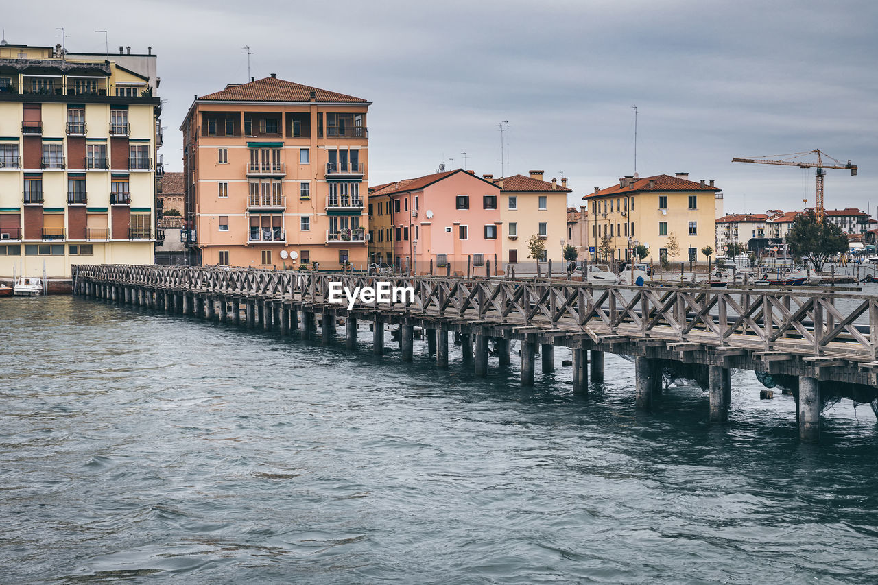 BRIDGE OVER RIVER BY BUILDINGS AGAINST SKY