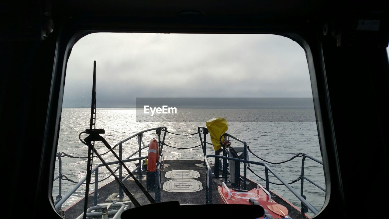 Scenic view of sea against cloudy sky seen through glass window of lifeboat