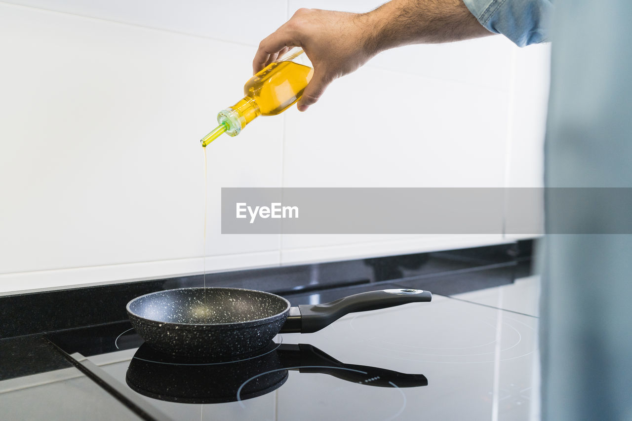 Man cooking in the kitchen in a denim shirt. an anonymous man is pouring olive oil into the pan