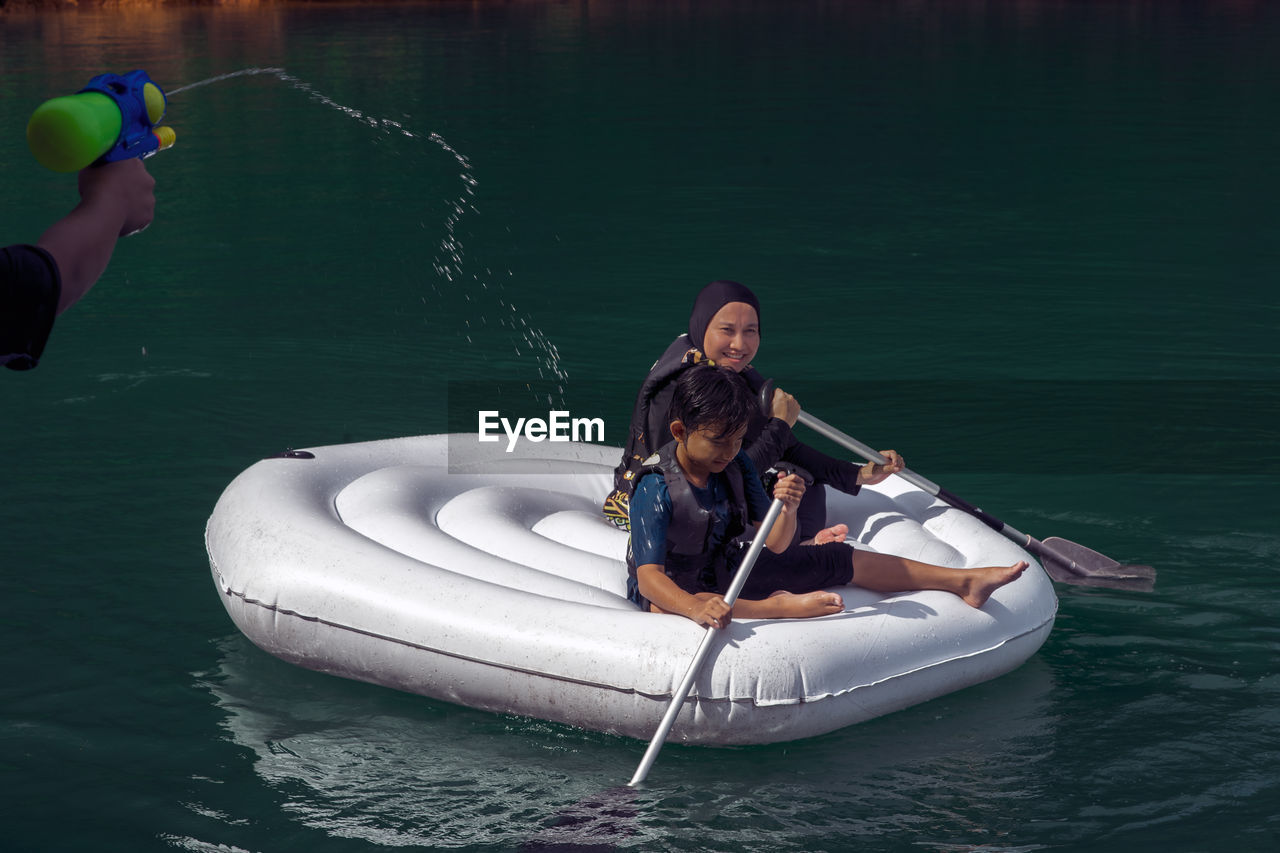 Boy spraying water on people in boat on sea