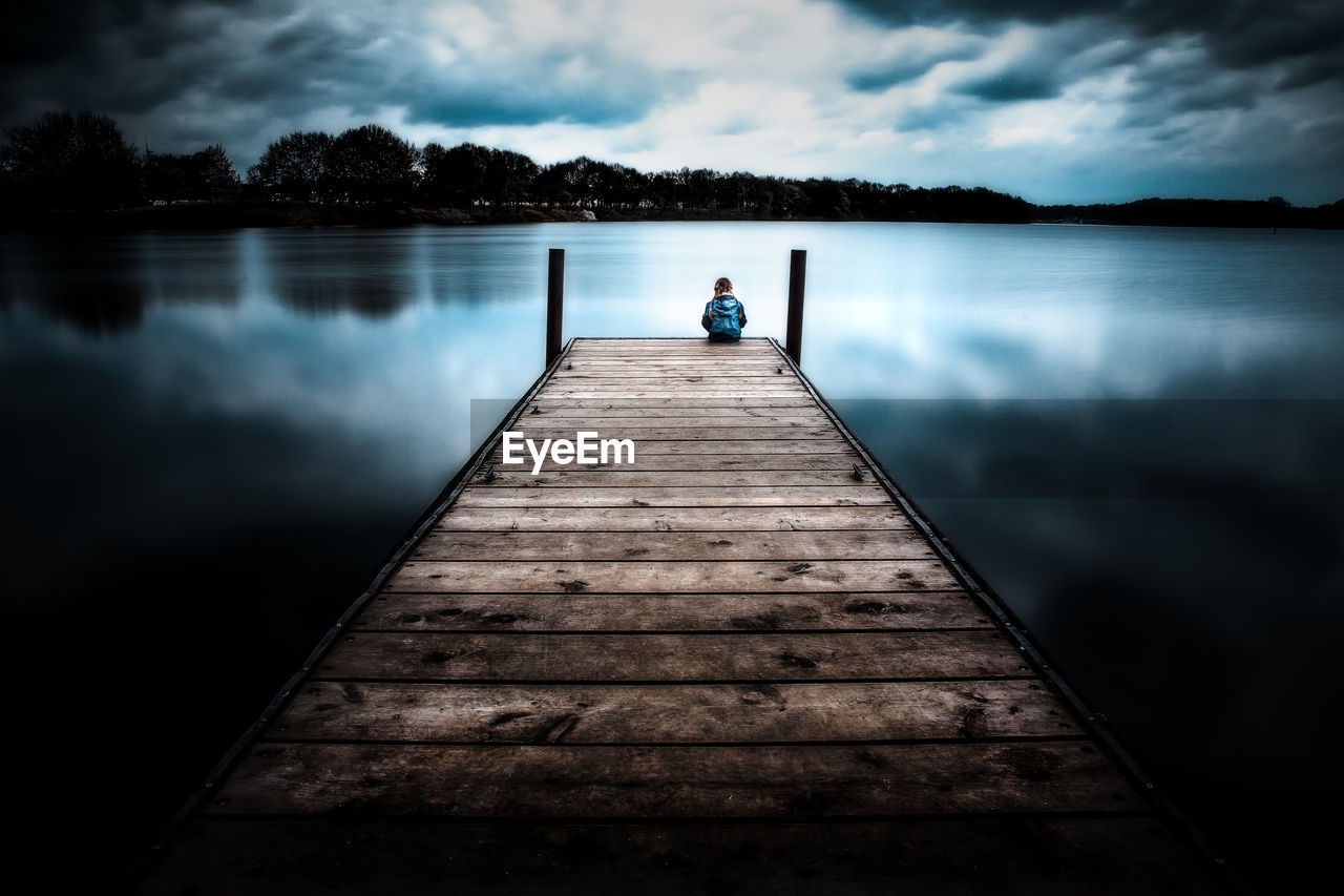 Rear view of girl sitting on pier over lake