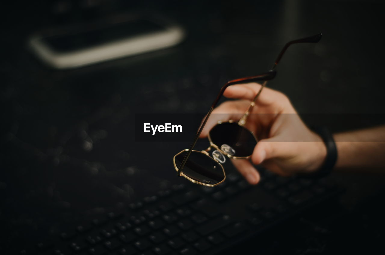 Cropped hand of man holding sunglasses over keyboard at table