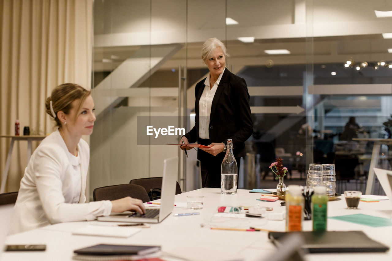 Mature professional discussing strategy while female colleague using laptop in global business meeting