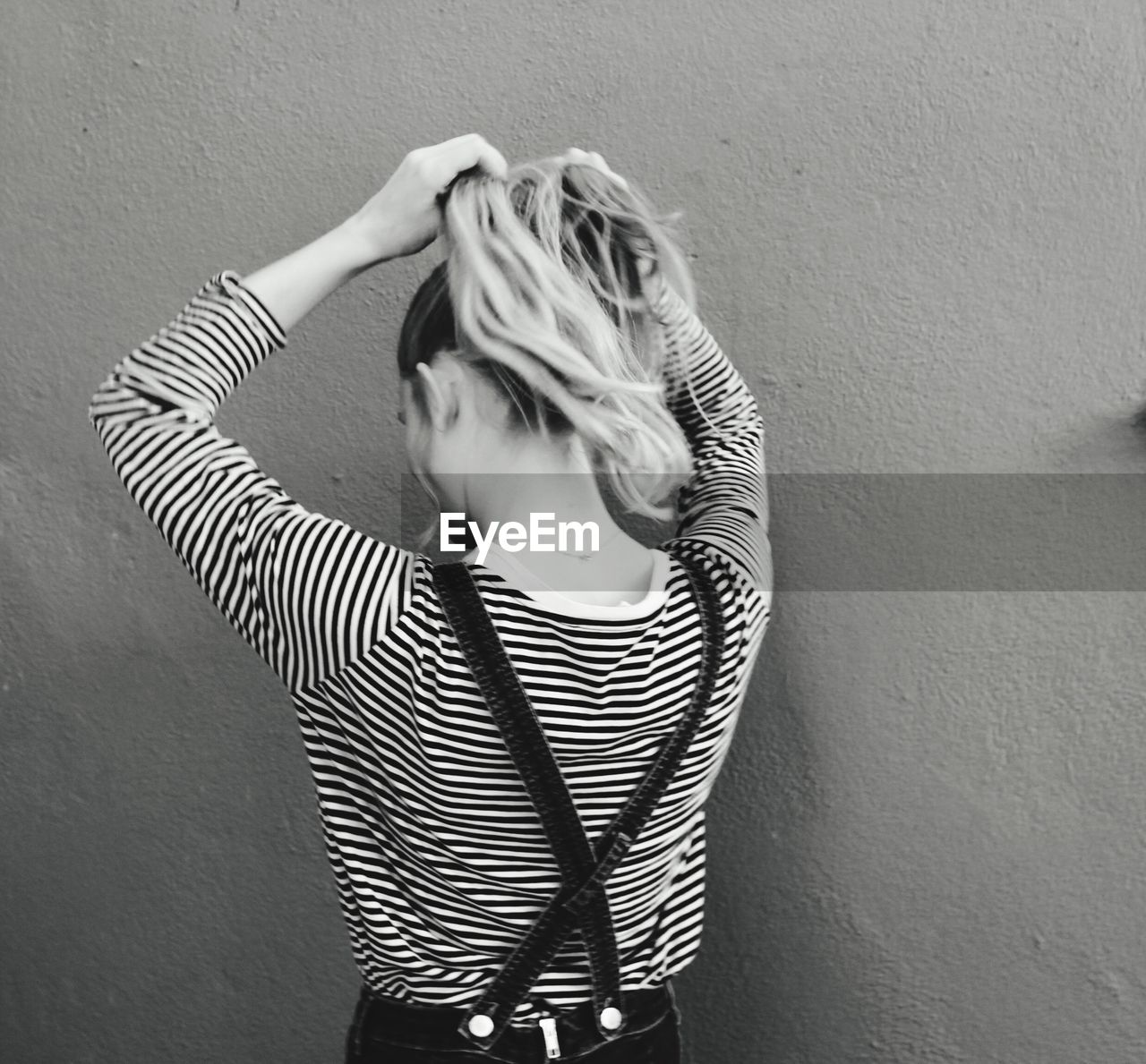 YOUNG WOMAN STANDING AGAINST WALL IN BACKGROUND