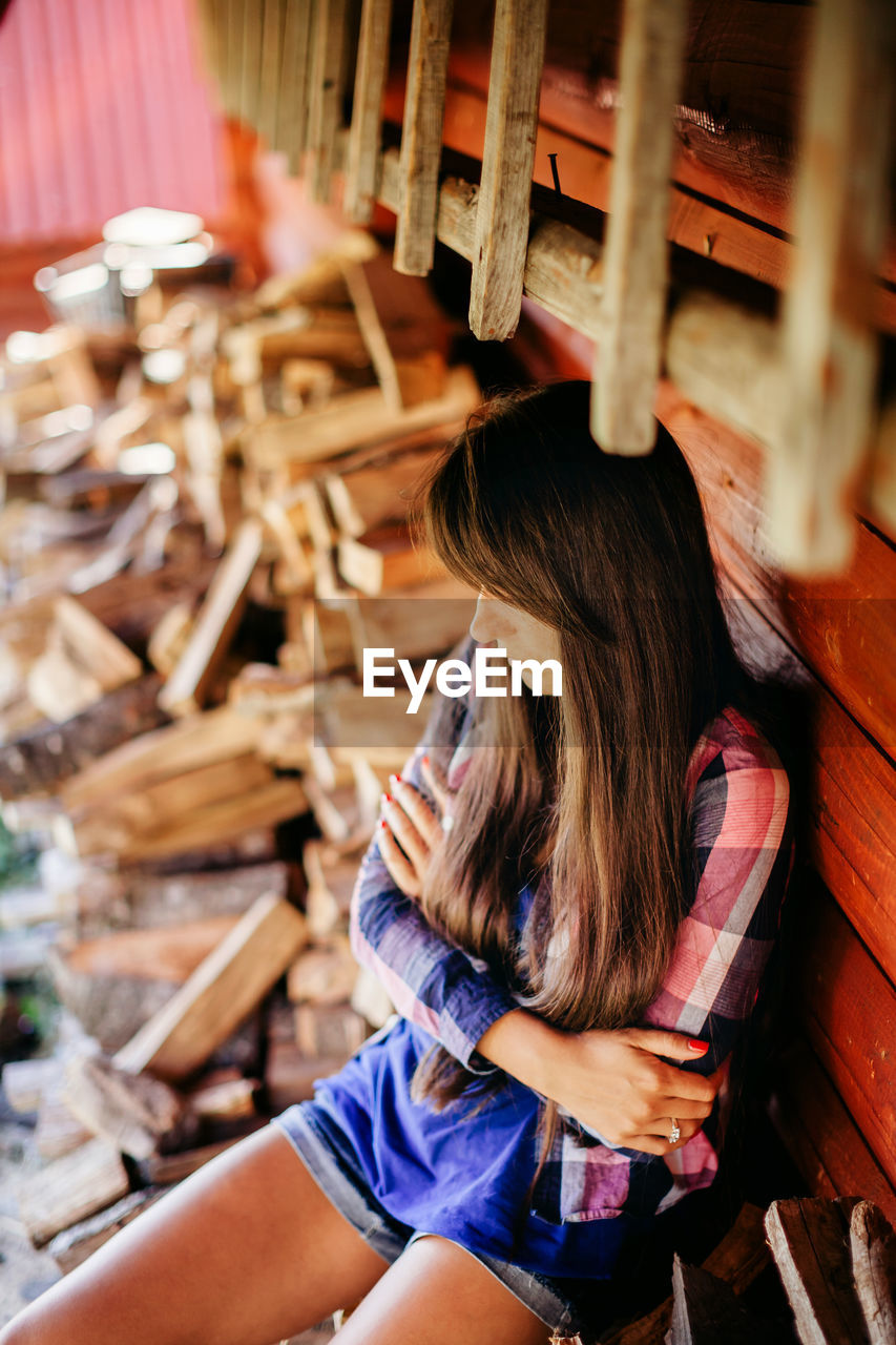 High angle view of woman sitting by stacked logs