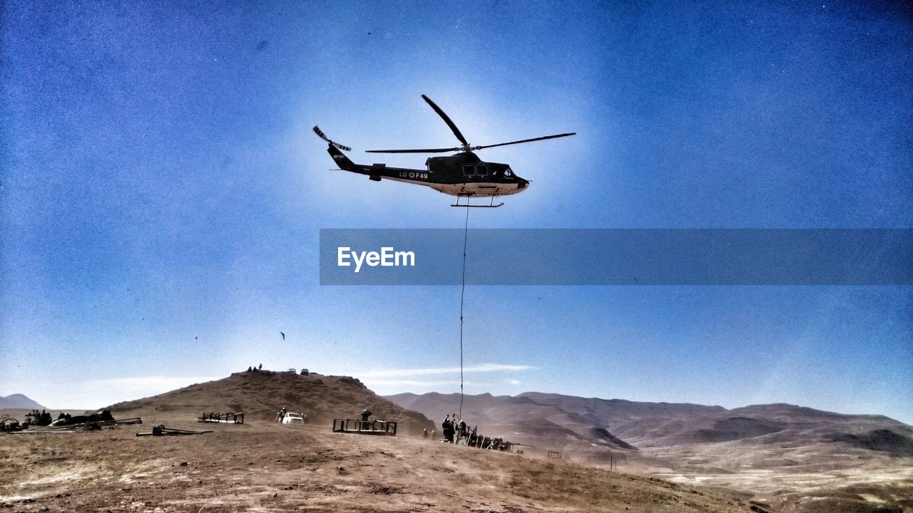 Helicopter flying over landscape against blue sky