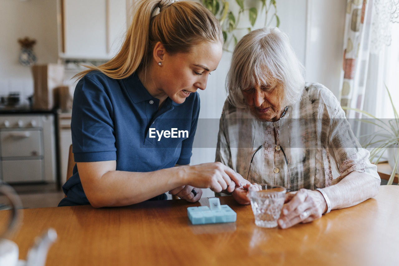 Female caregiver assisting senior woman while taking medicines at home