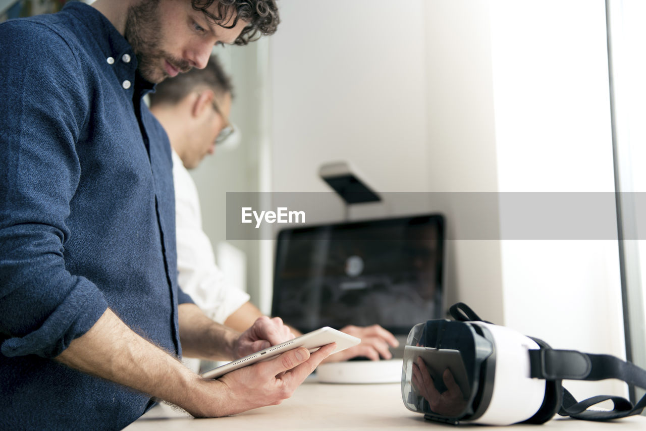 Engineer using tablet computer while colleague using computer in office