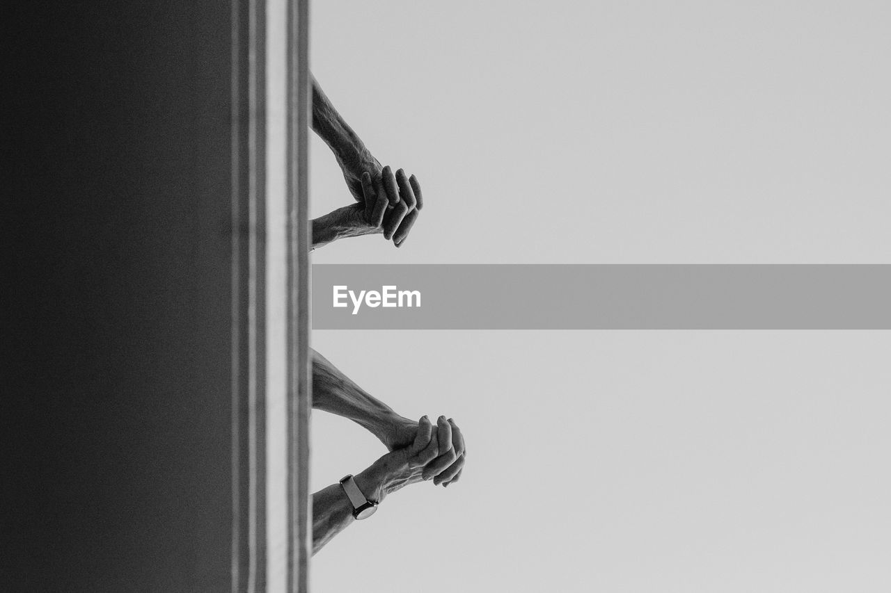 Cropped image of hands clasped against clear sky