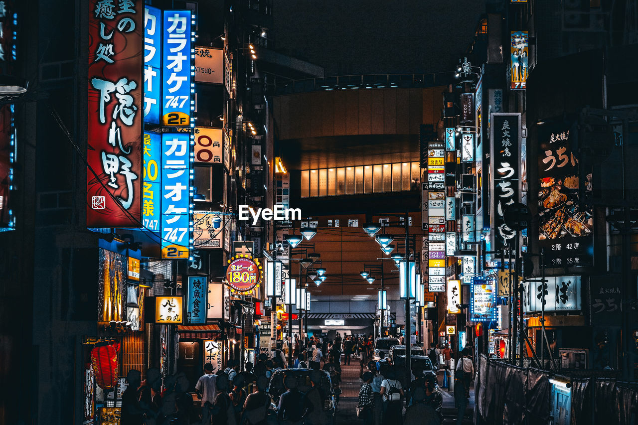 PEOPLE ON ILLUMINATED STREET AT NIGHT IN CITY