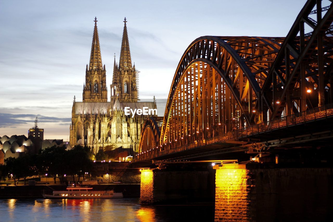 Cologne cathedral and illuminated hohenzollern bridge against sky during sunset