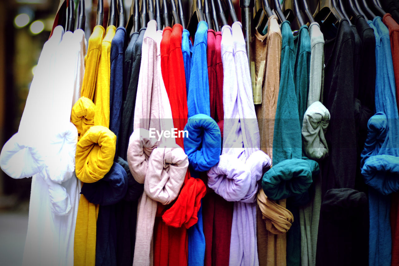 CLOSE-UP OF MULTI COLORED CLOTHES HANGING AT STORE