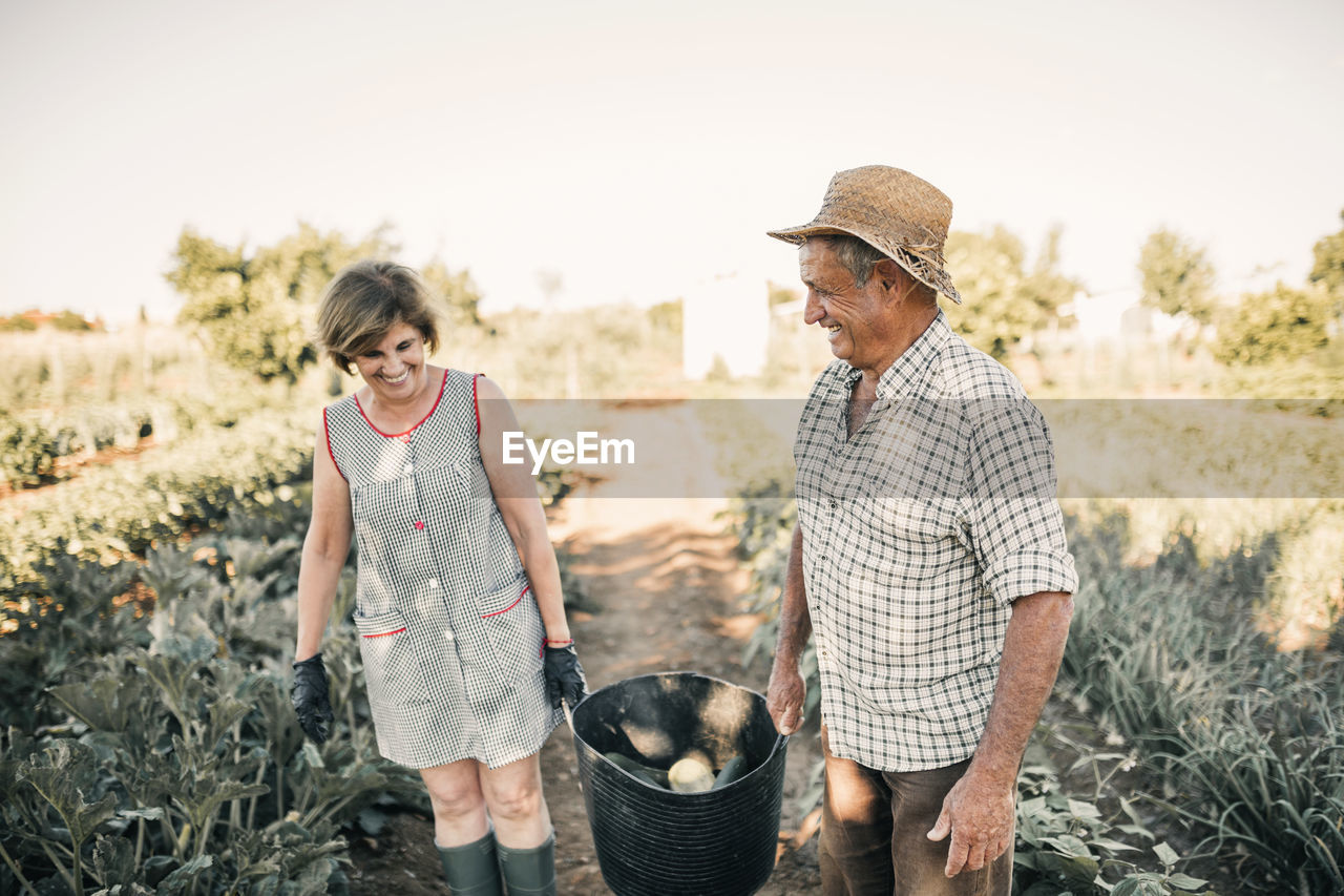 Smiling senior couple holding vegetable basket at farm