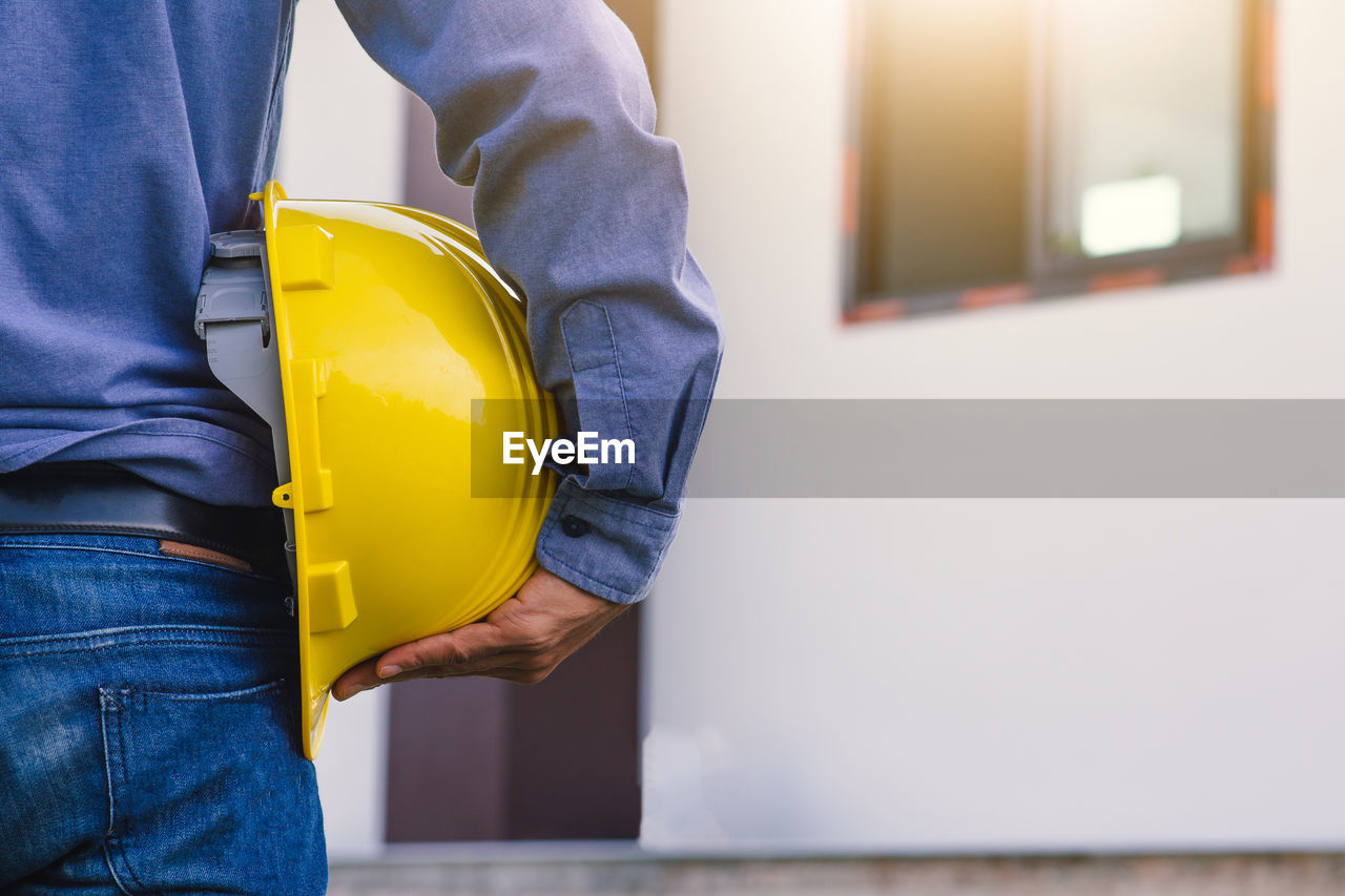 MIDSECTION OF MAN WORKING WITH YELLOW MACHINE