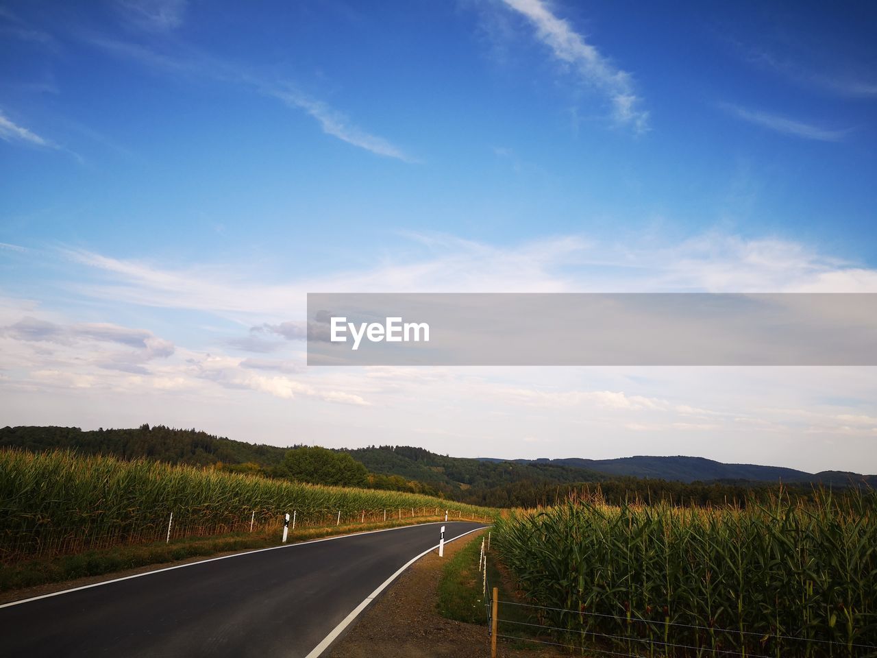 Empty road amidst field against sky