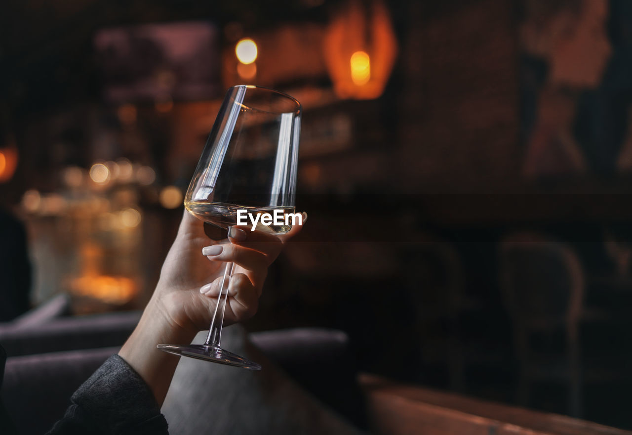 Female hand with french manicure holding a glass with wine on naturally blurred background