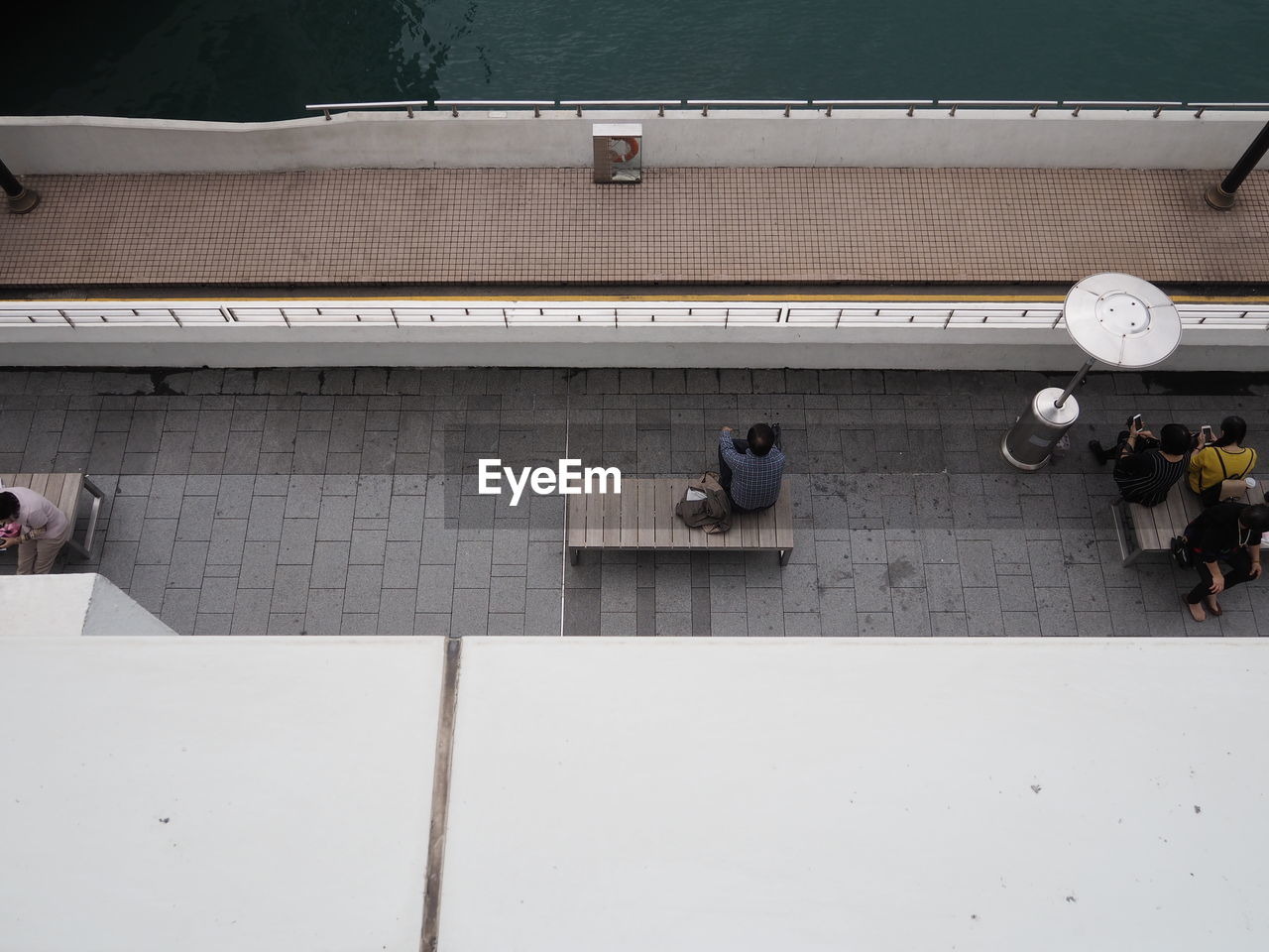 High angle view of people sitting on bench at sidewalk