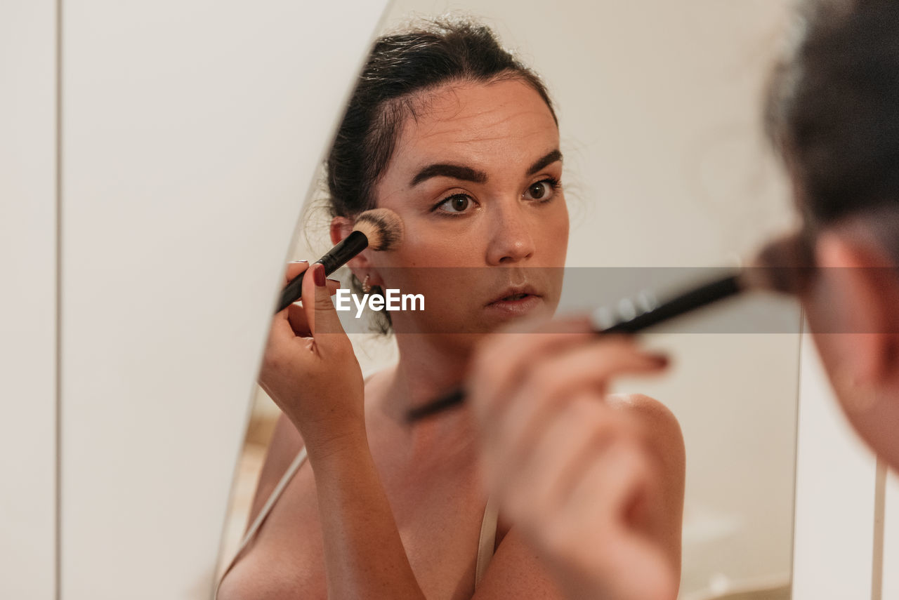 Mirror photo of beautiful young woman putting on makeup