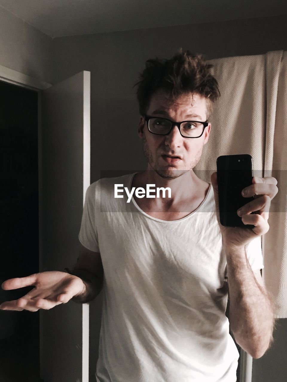 Mid adult man taking selfie with smart phone reflecting on mirror at home