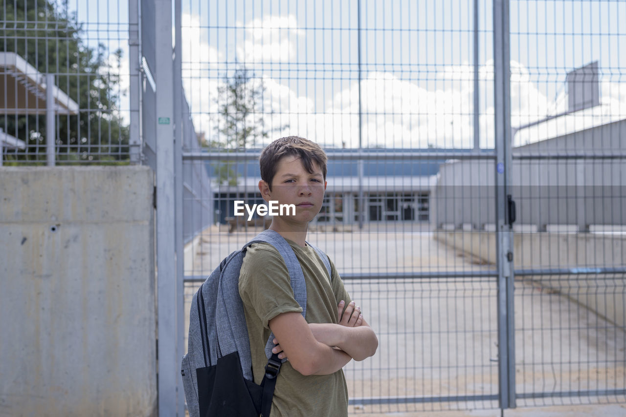 Portrait of confident boy with arms crossed standing against metal gate