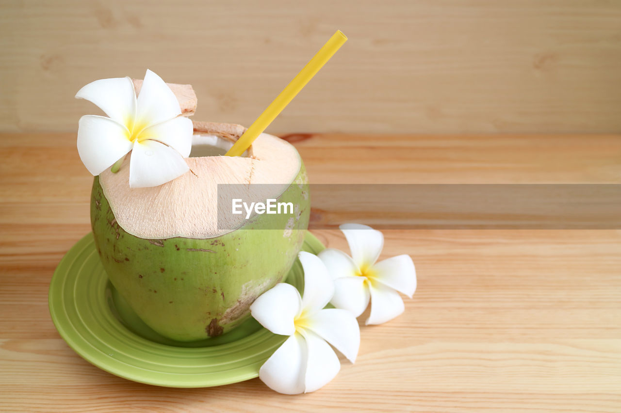 Fresh young coconut juice with frangipani flowers served on wooden table