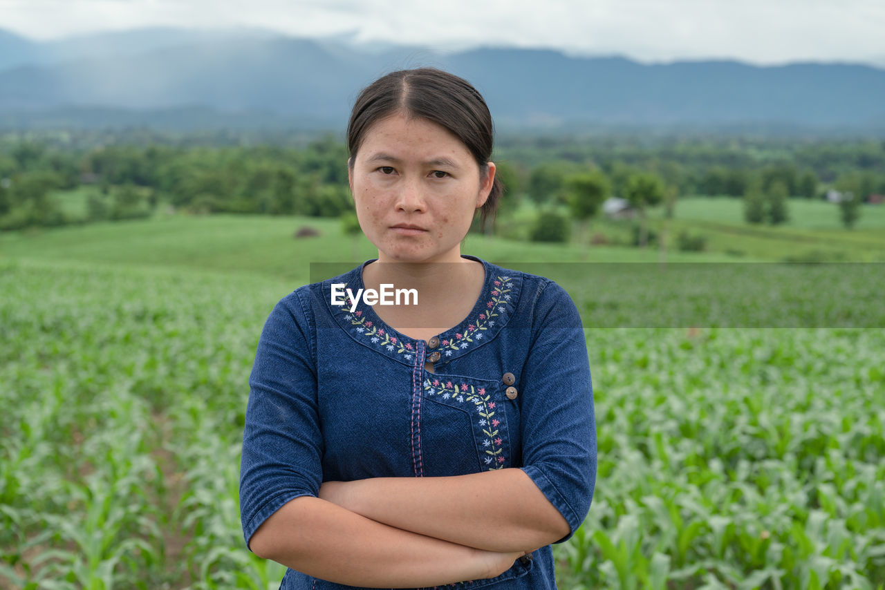 Portrait of young woman standing with arms crossed on field