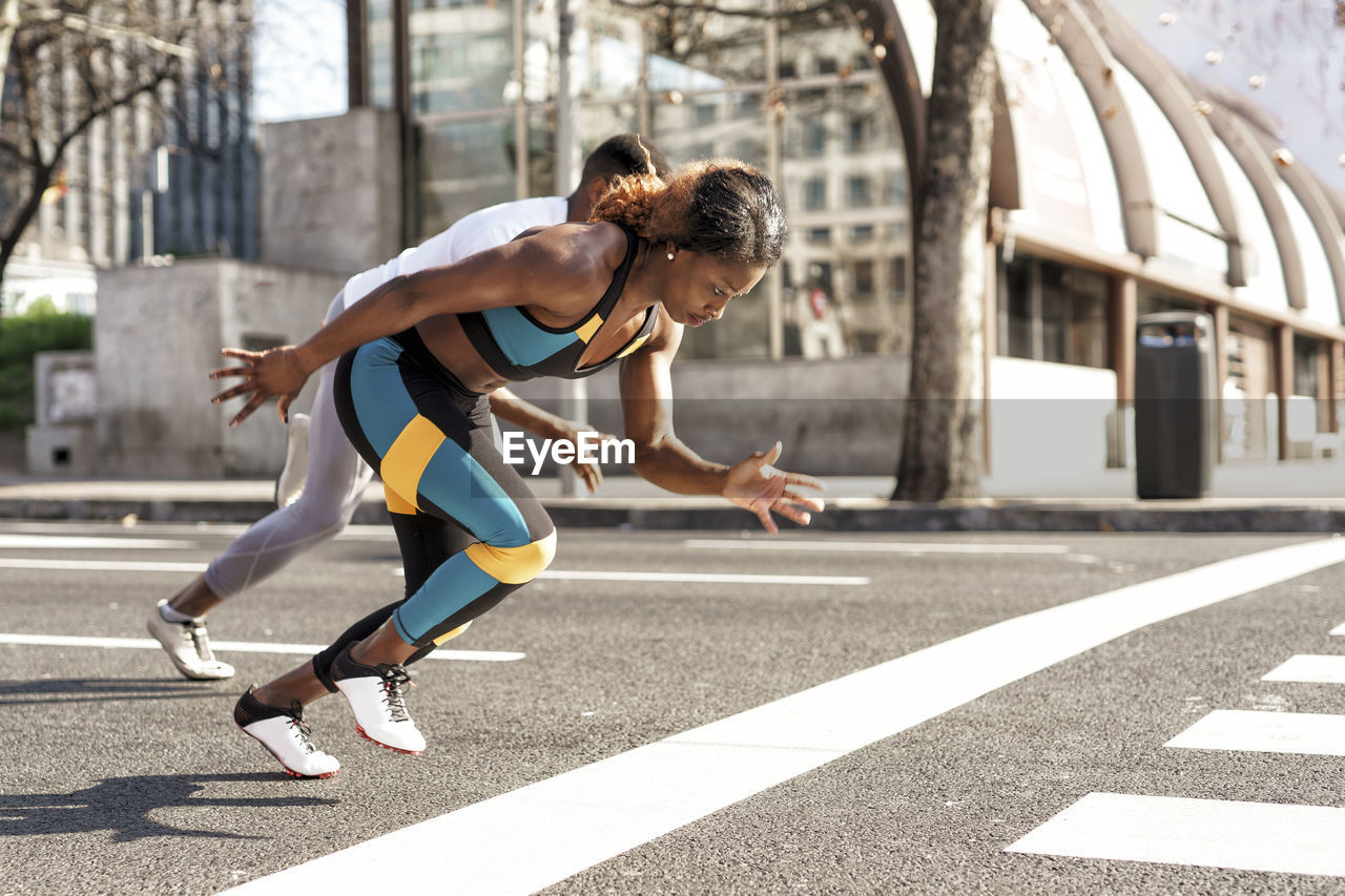 Young man and woman practicing for sports race while running in city