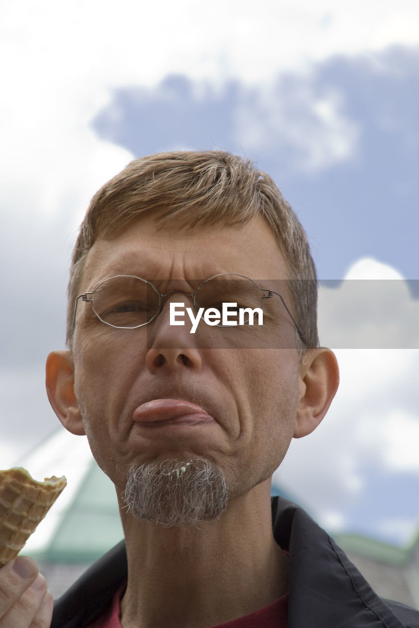 Portrait of mature man sticking out tongue against sky