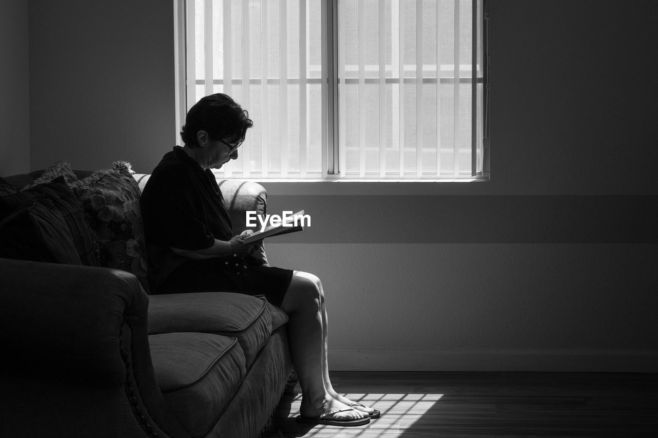 Silhouette mature woman reading book while sitting on sofa at home