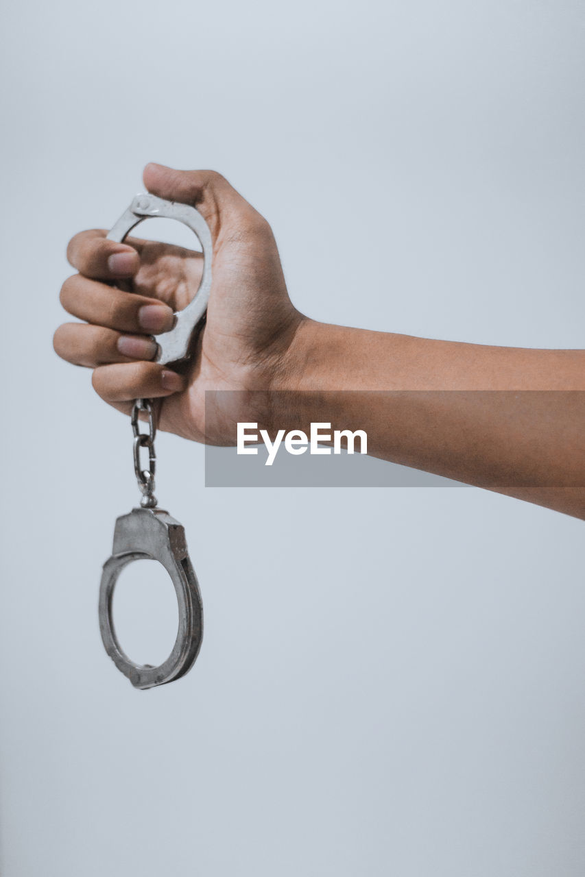 Close-up of hand holding handcuffs against white background