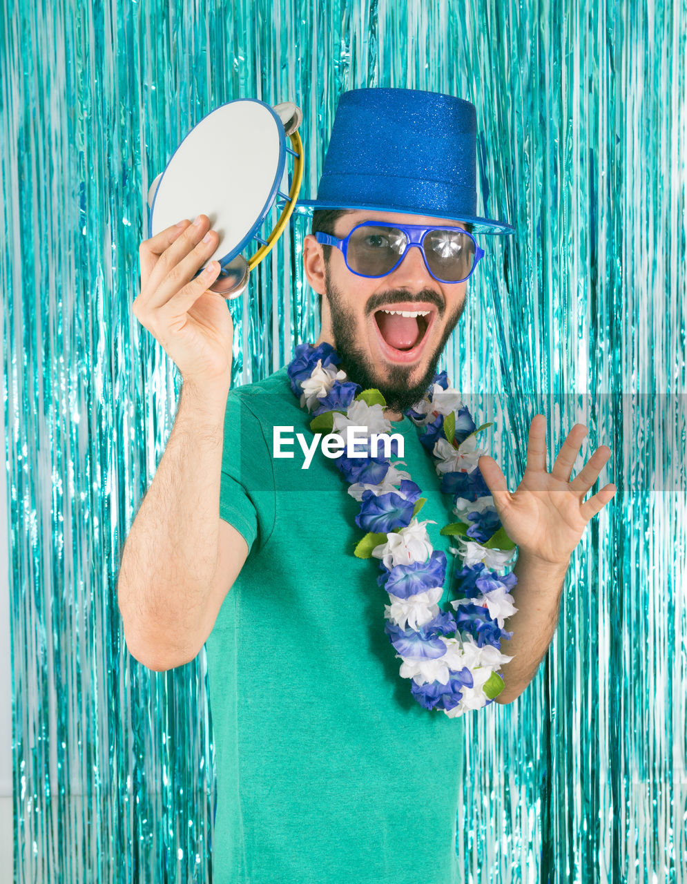 Portrait of happy man holding pandeiro against wall