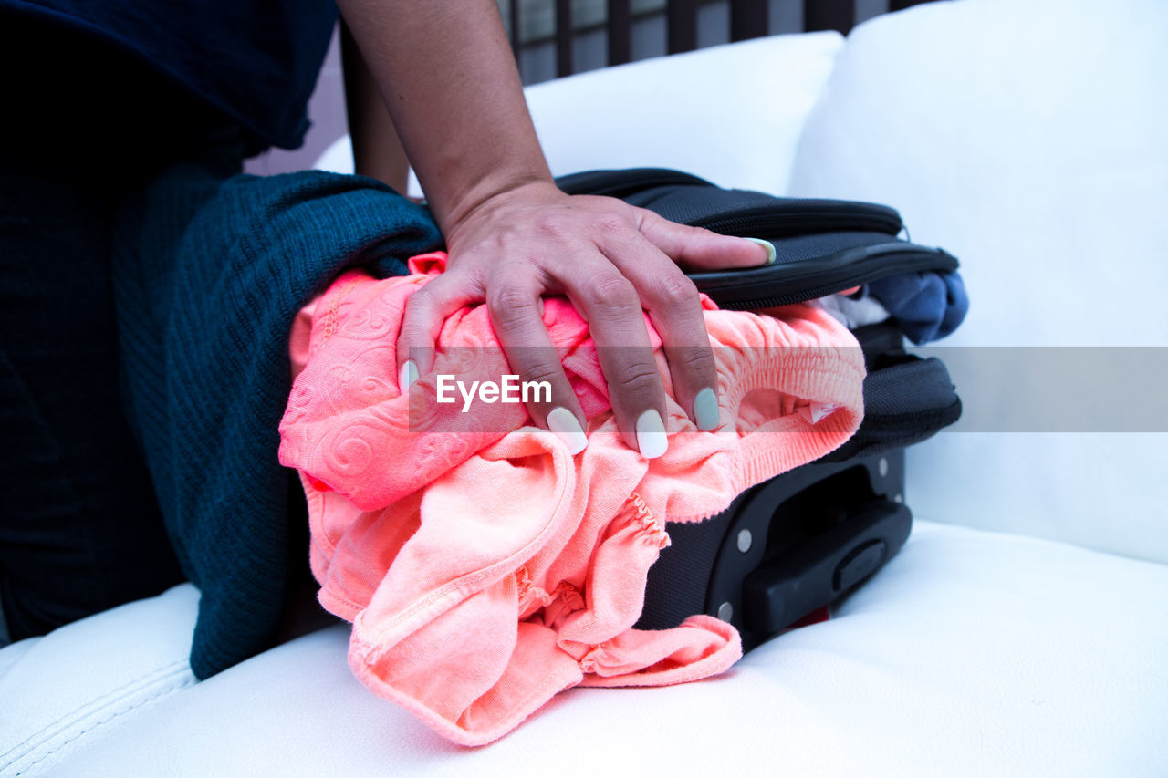 Midsection of woman packing overburdened bag on sofa