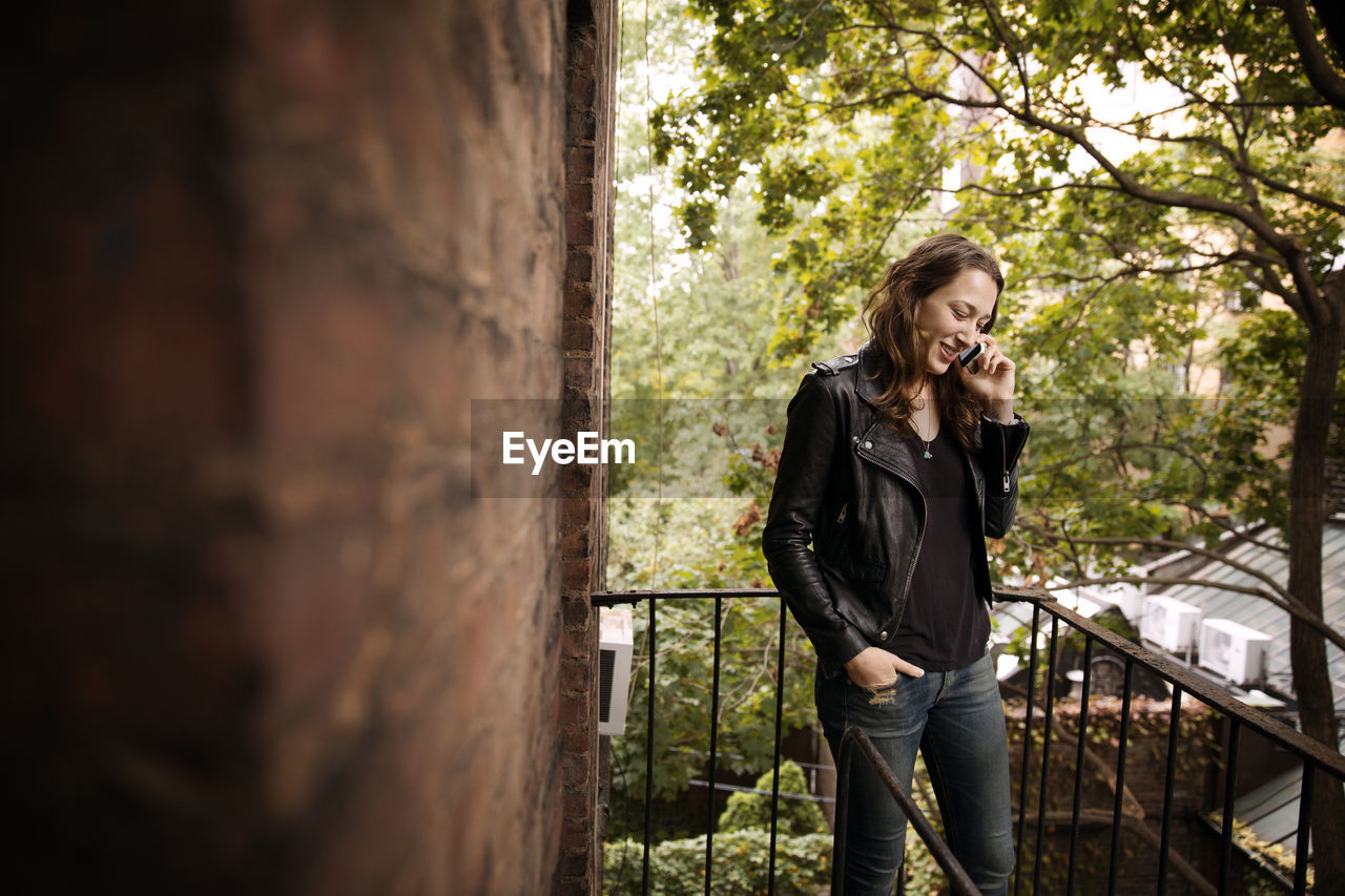 Smiling woman talking on phone while standing at fire escape