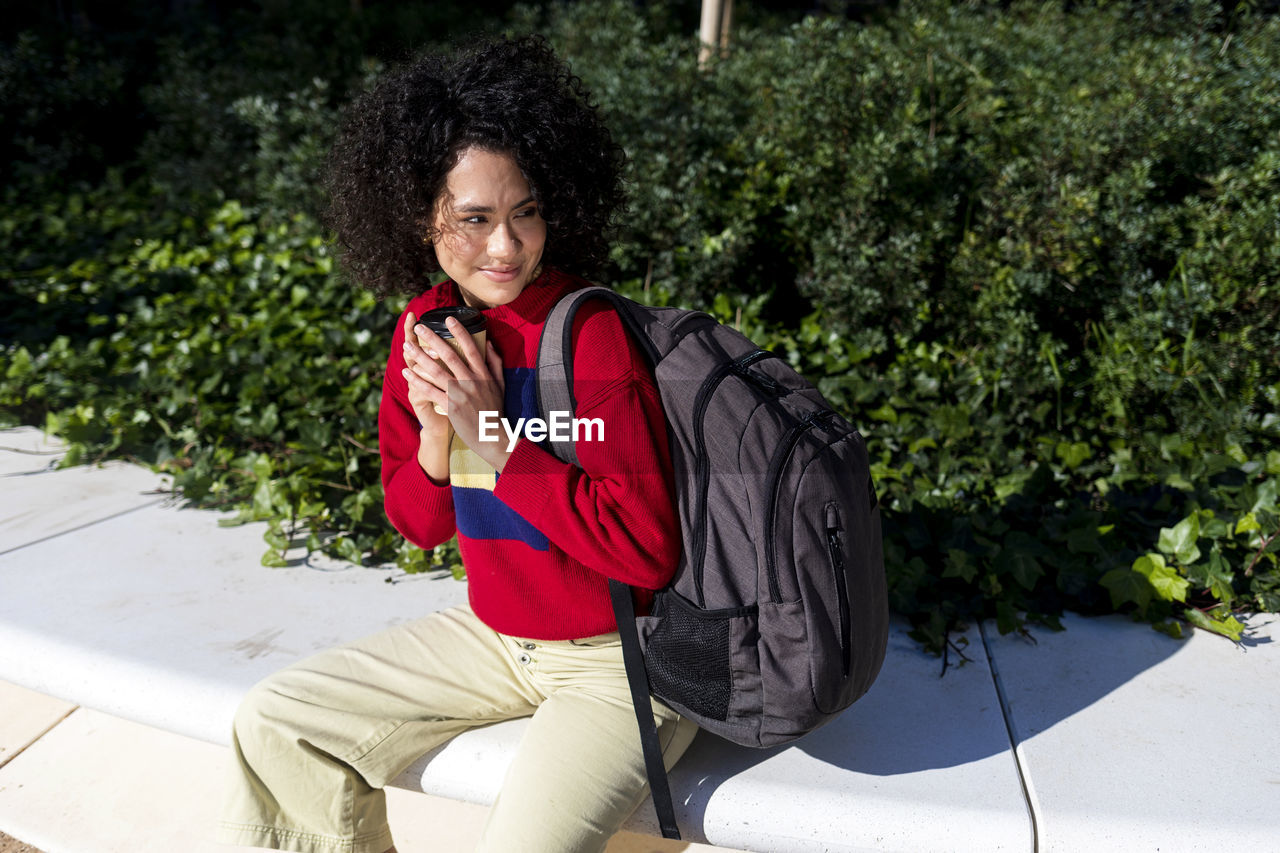 Woman looking away while sitting against plants