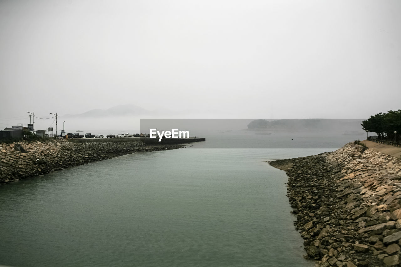 Groynes at coastline against sky in foggy weather