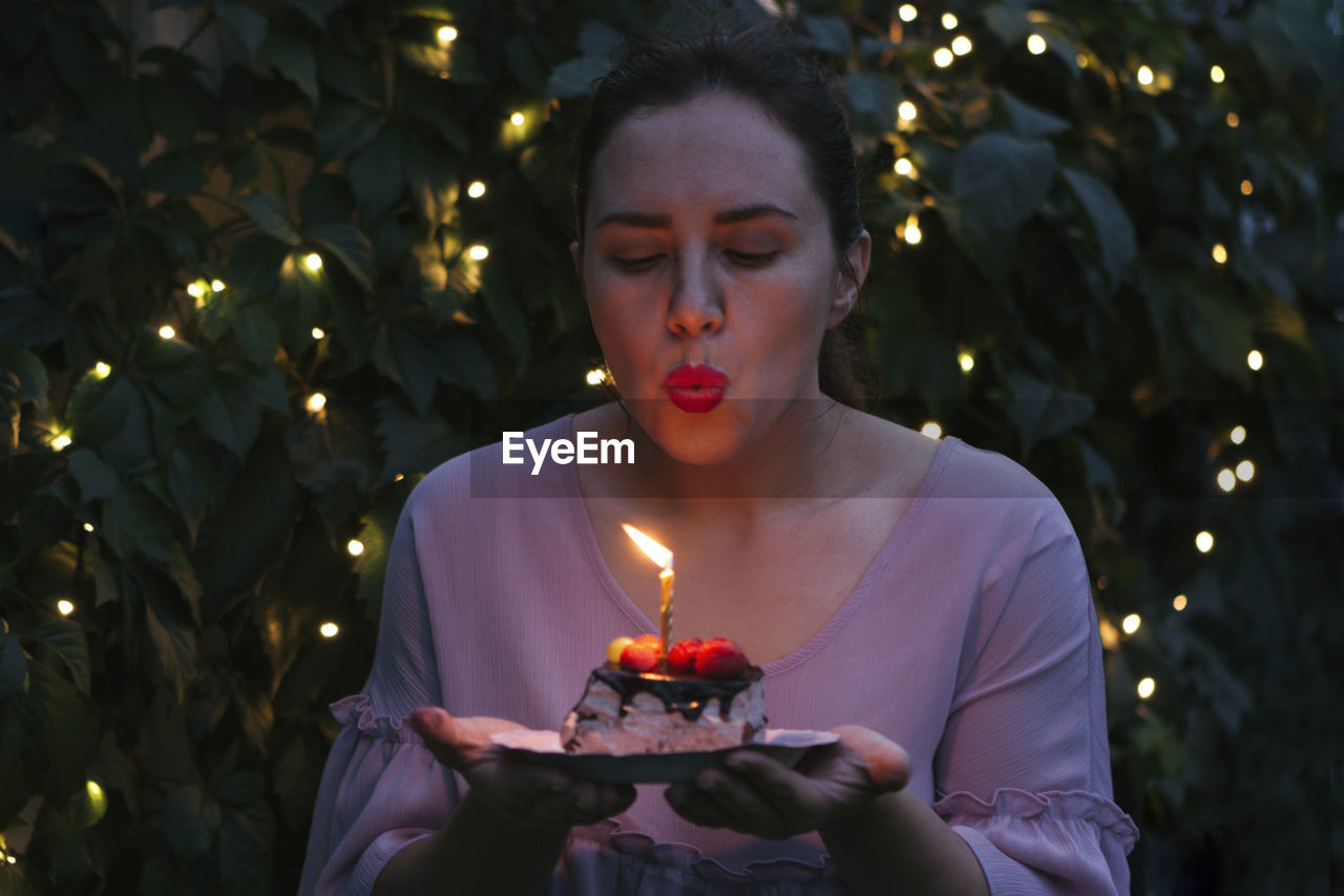 Woman blowing on piece of cake with birthday candle