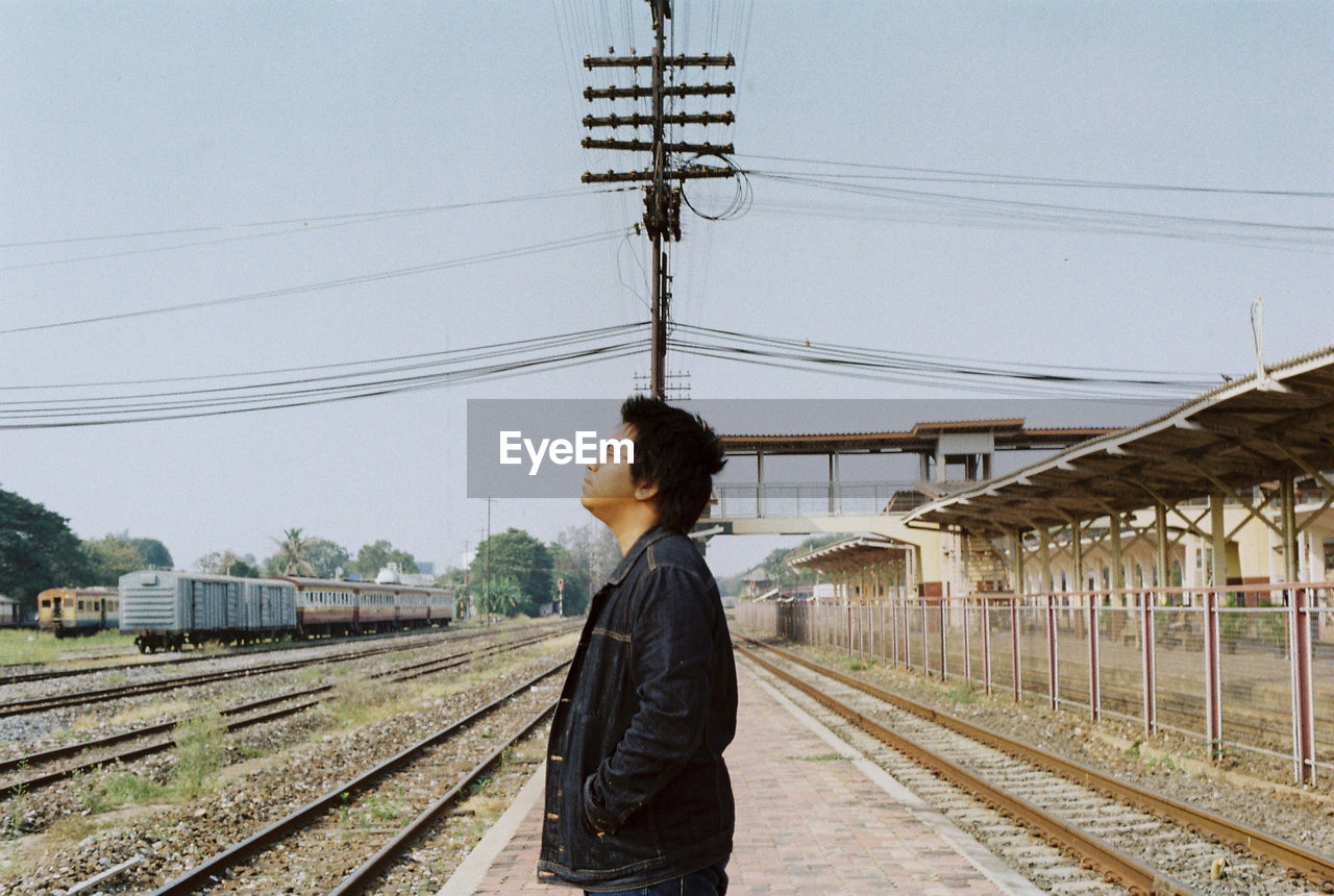 Side view of man standing at railroad station against sky